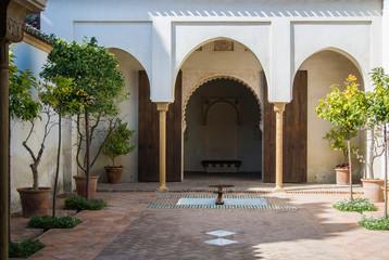 Fototapeta premium A quiet yard at Alcazaba, a castle of Malaga, with orange trees at pots, fountains and arch entrance in arab style, Andalusia, Spain.