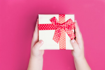 White gift box with red bow in the children's hands on pink backgroundclose up