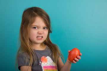 Little girl with displeased expression holding tomato