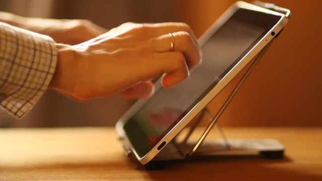 A man swiping and typing on a tablet pc touchscreen. Man's hands in contre-jour close-up
