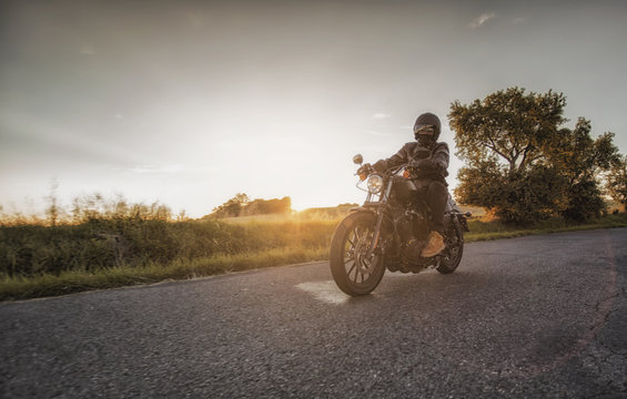 Fototapeta Biker rides his motorcycle along the road during beautiful sunset. Motorbiker's season starts now during spring time.