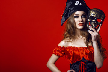 Portrait of gorgeous sexy woman with provocative make-up in pirate costume holding skull mask next...