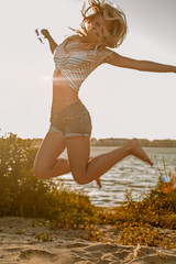 Happy girl jumping on summer beach shot with sun flares retro color, motion blur selective focus