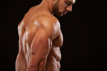 Fototapeta premium Strong Athletic Man - Fitness Model showing his perfect back isolated on black background with copyspace