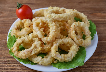Fried calamari rings with lettuce on wooden background