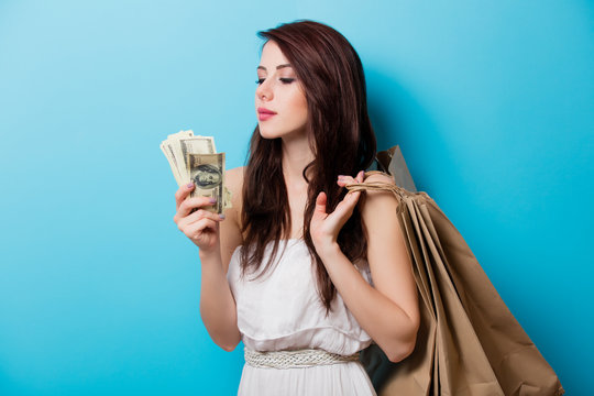 beautiful young woman with shopping bags and money standing in front of wonderful blue background