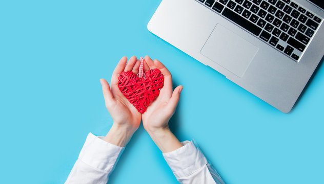 White Caucasian Female Hands Holding Heart Shaped Toy Near Laptop On The Wonderful Blue Background