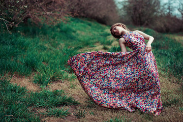 Portrait of a young blond woman on a background of spring trees. girl spinning. pink dress fluttering in the wind