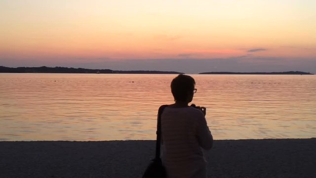 Woman shoots calm see after sunset. Brijoni Island seen in the distance