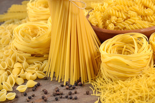 Assortment of uncooked Italian pasta and black pepper on a wooden background