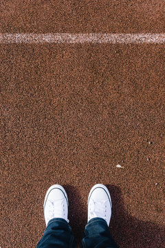 Legs on red tartan sports field with two shoes, personal perspective from above