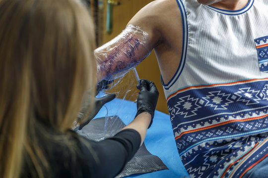 A blonde tattooist is covering a tattoo on a boy´s arm
