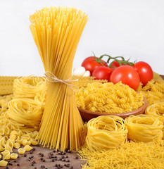 Uncooked Italian pasta, ripe tomatoes branch and black pepper on a white