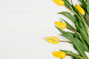 Background with yellow tulips on white wooden table top view. Creative woman's workspace concept with copy space. Product photograph taken from above with frame composition