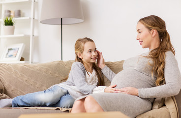 happy pregnant woman and girl on sofa at home