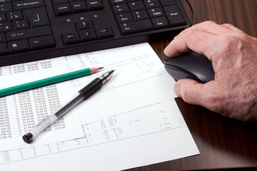 Keyboard, mouse in man's hand, papers, pen and pencil on the table