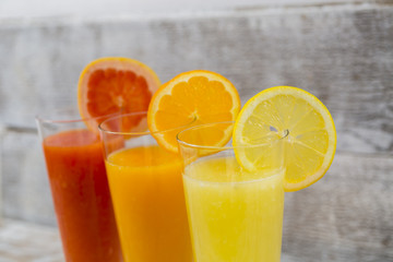 Citrus juices in glass and a slice of  lemon, grapefruit and  orange on wooden background .