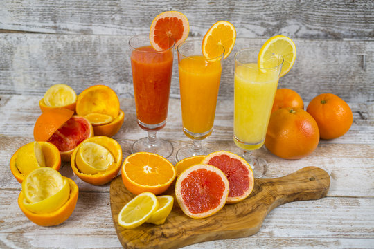 Citrus juices in glass and a slice of  lemon, grapefruit and  orange on wooden background .
