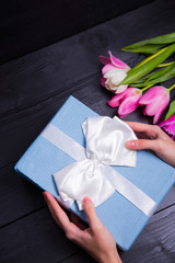 Bouquet of tender pink tulips with gift box on black wooden background