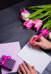 Obraz premium Female hands writing on clear paper with gift box and bouquet of tulips