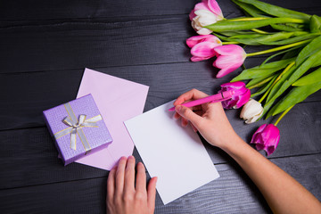 Female hands writing on clear paper with gift box and bouquet of tulips