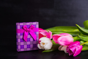 Bouquet of tender pink tulips with gift box on black wooden background