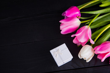 Bouquet of tender pink tulips with gift box on black wooden background