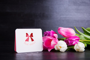 Bouquet of tender pink tulips with greeting card on black wooden background
