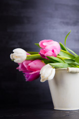 Bouquet of tender pink tulips in vintage pail on black wooden background