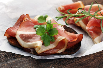 Bread with slices jamon serrano for lunch table. Sharing antipasti on party or summer picnic time over wooden rustic background.