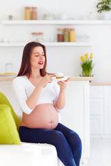 Obraz na płótnie Canvas beautiful pregnant woman eating tasty sweet cakes at home