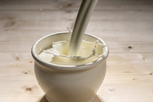 Milk is poured into a clay jar with a splash on a wooden table