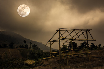 Bamboo hut and mountain peaks. Silhouettes of trees with sky and full moon.