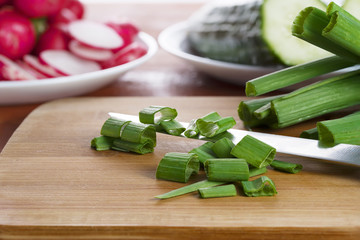 Young green onions cut by rings on a wooden board, prior to the treatment in lettuce