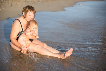 Naked baby on aged woman hands at beach