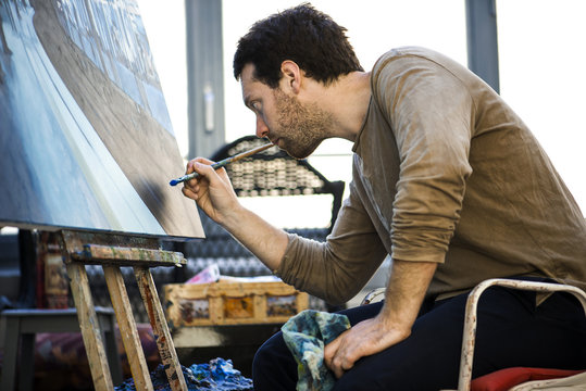 Young man painting while sitting indoors