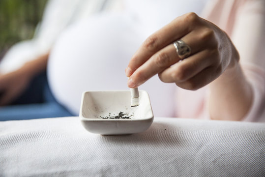 Pregnant woman putting cigarette out in ashtray