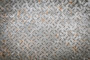 Old metal floor plate with diamond pattern and rusty background texture.