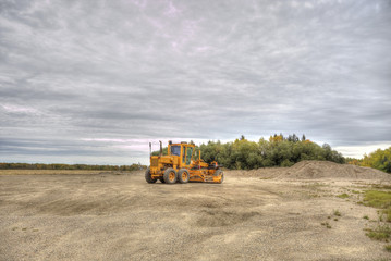 Fototapeta premium An orange industrial gravel road grader parked at a small gravel pit by an autumn forest in a rural countryside landscape
