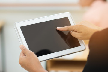 teacher hand holding use tablet with blurred student in classroom background, education concept