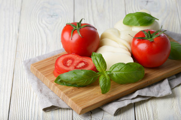 Mozzarella and tomato with basil leaves on a white wooden background