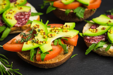 Sandwiches with salami, avocado and herbs on the black stone background