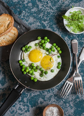 Delicious breakfast - fried eggs with green peas. On a dark background, top view