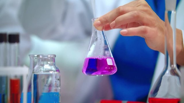 Lab scientist pouring liquid in lab flask. Close up of female scientist doing laboratory experiment. Lab worker hands doing laboratory testing with chemical liquid in beaker