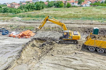 Excavator is digging a trench and loading a truck on building site