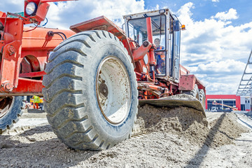 Grader is leveling ground at construction site, view on undercarriage