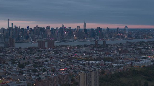 ESTABLISHING AERIAL SHOT: Flying over New Jersey residential area towards famous New York City skyline after the sunset. Magical city lights shining in lit up Jersey City and NYC financial district