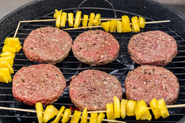 Grilled meat on a charcoal griddle accompanied by onions in foil and pineapple.