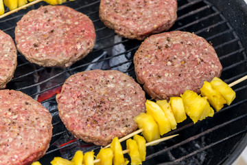 Grilled meat on a charcoal griddle accompanied by onions in foil and pineapple.