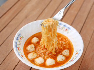 Instant noodles with meat balls in ceramic bowl against wooden plank.